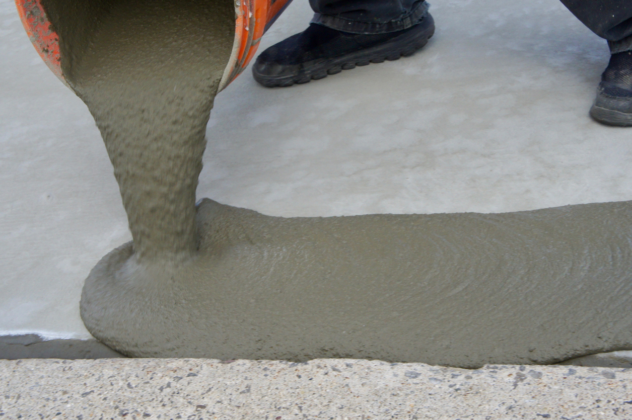 A worker applying a skim coat for concrete by pouring it out of a bucket